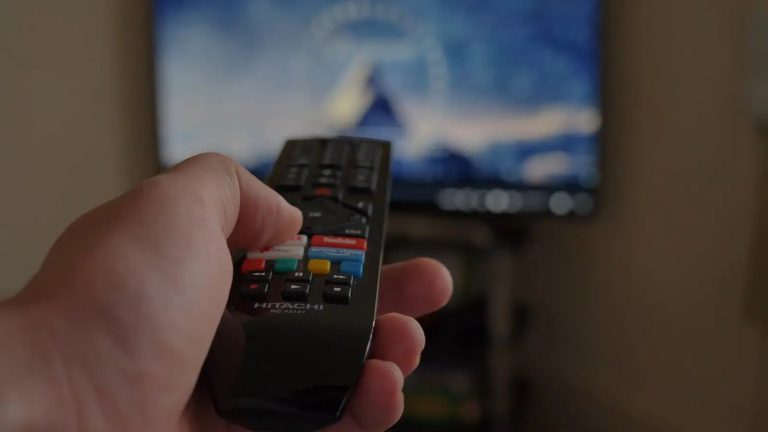 Main tenant une télécommande devant un téléviseur affichant un service de streaming